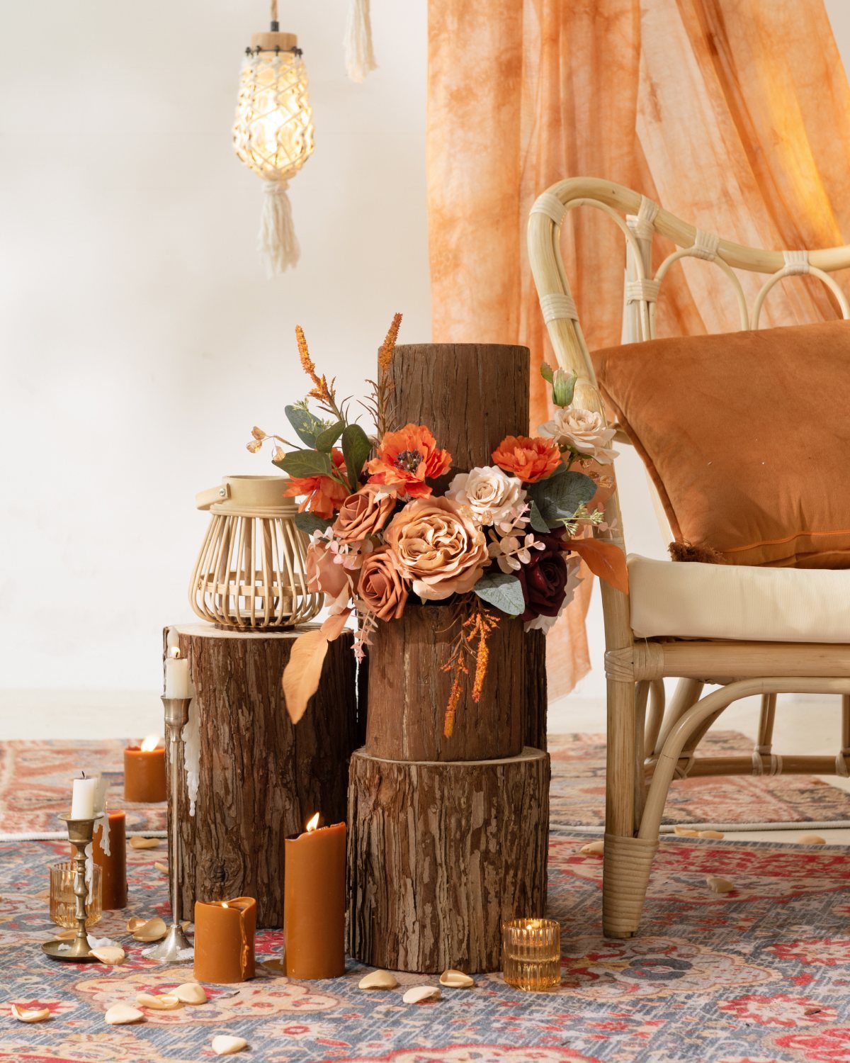 Terracotta floral arrangement on wooden logs with orange candles and rattan furniture.