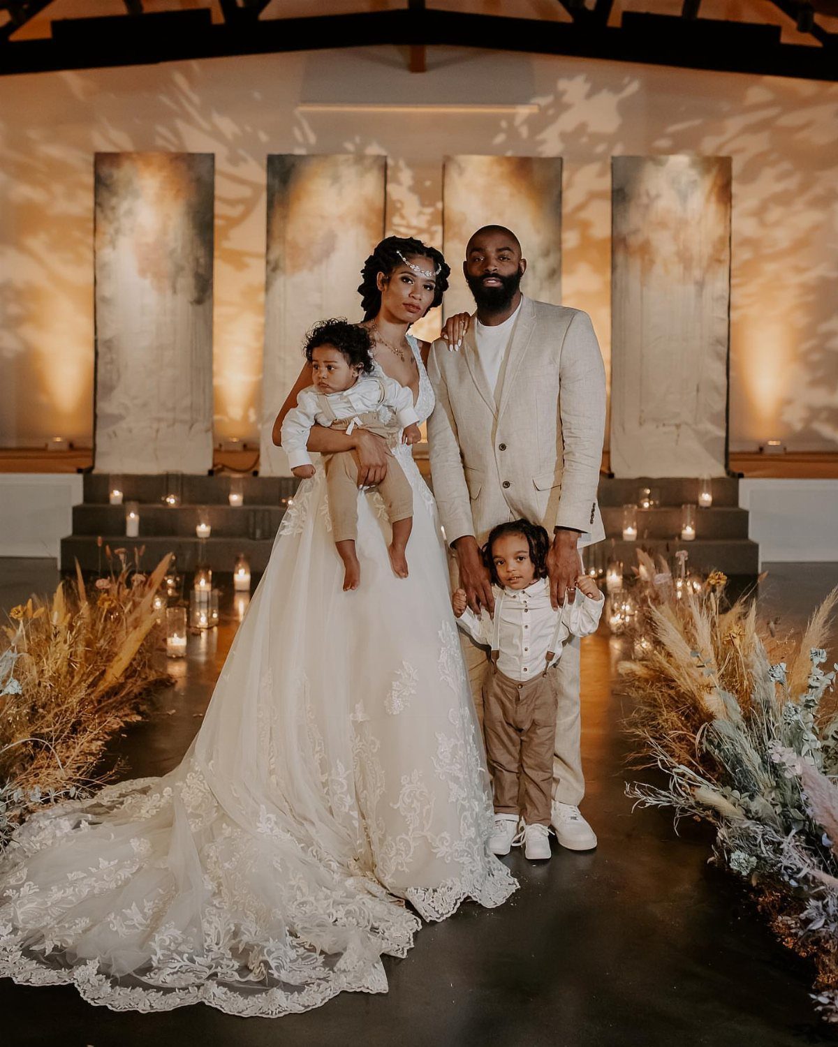 Family in wedding attire posing before abstract panels and candles in a venue.