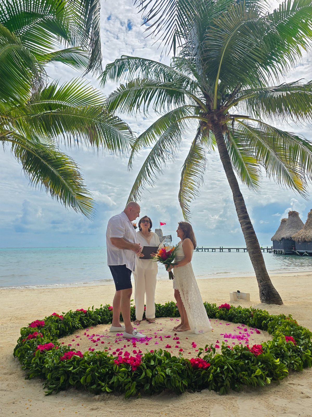 Couple exchanging vows on a tropical beach inside a pink floral circle.
