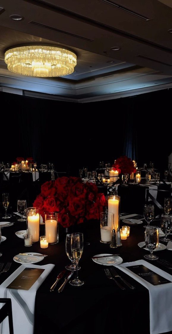 Elegant banquet table setting with red roses and glowing white pillar candles.