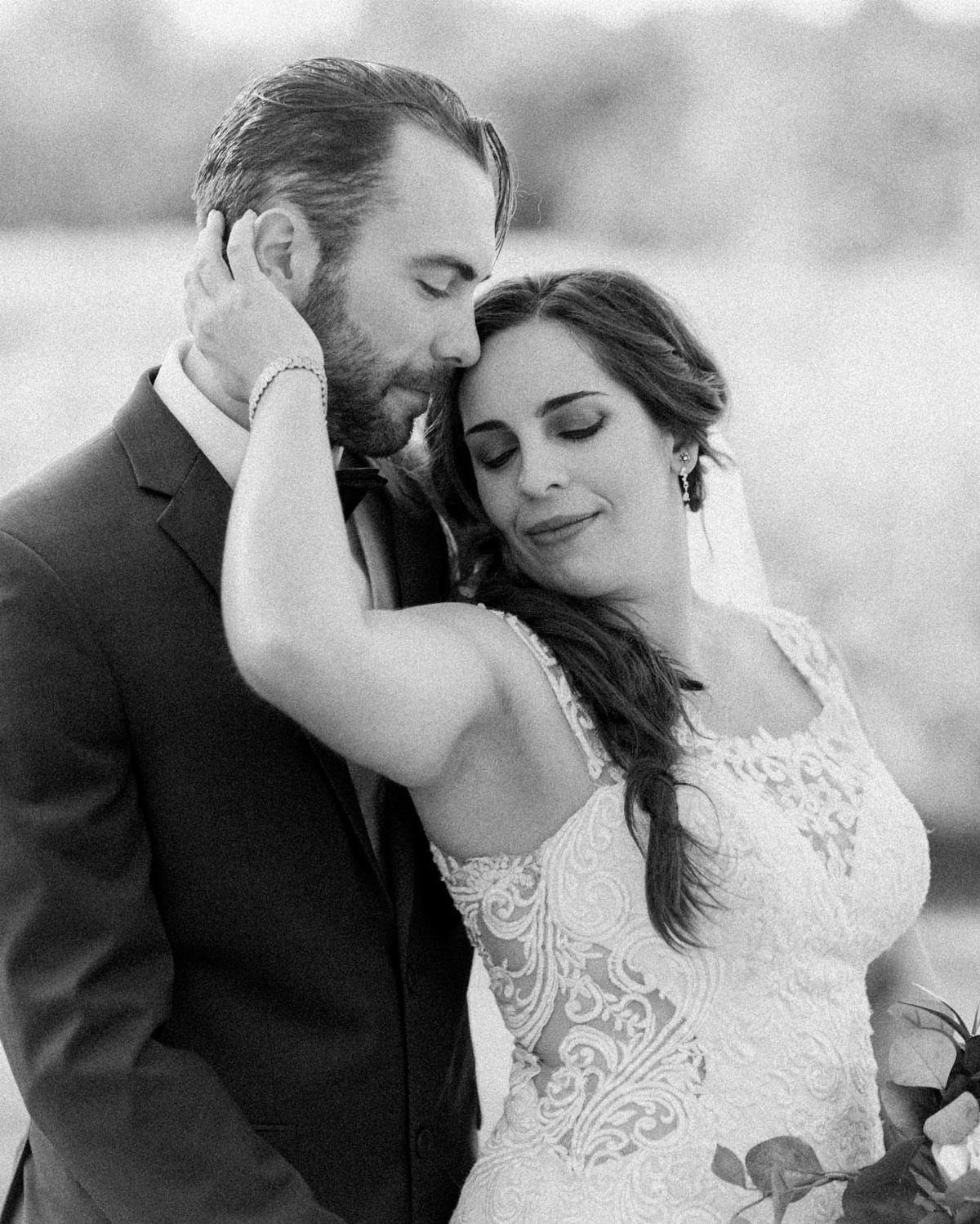 Couple in wedding attire embracing closely in a black and white portrait.