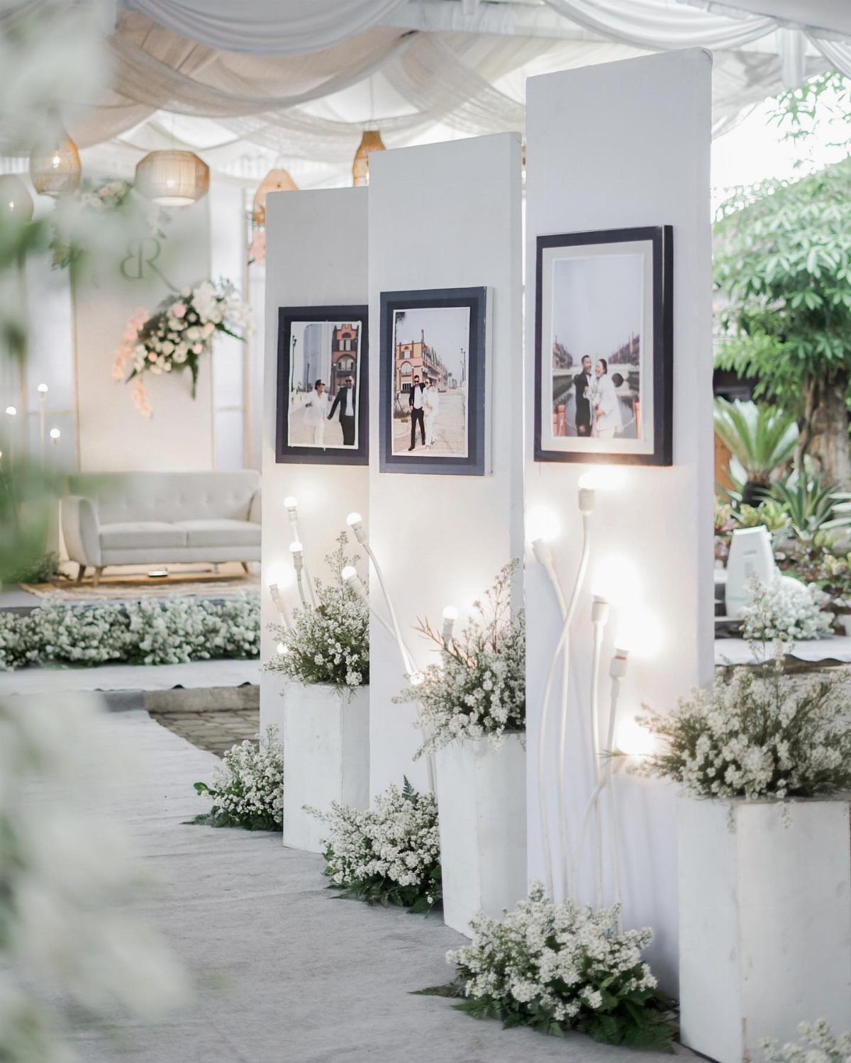 Framed wedding photos displayed on white panels with white flowers and soft lighting.