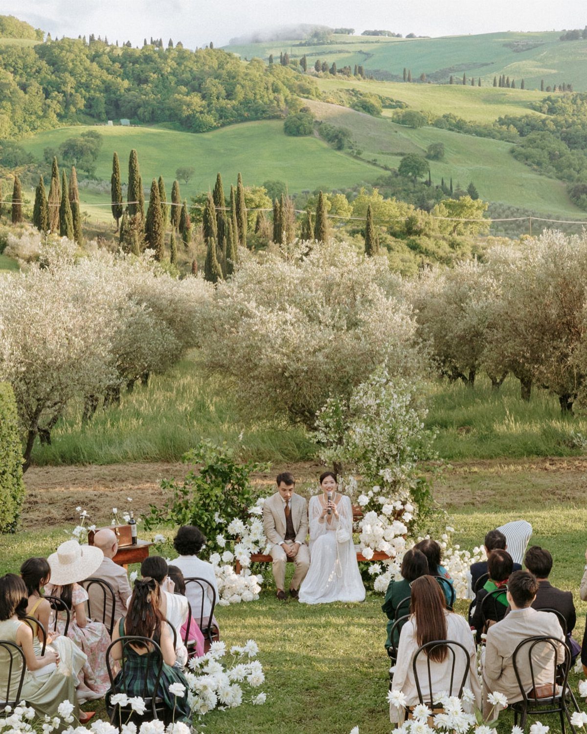 Couple standing under a white floral arch during an outdoor ceremony in Tuscany.