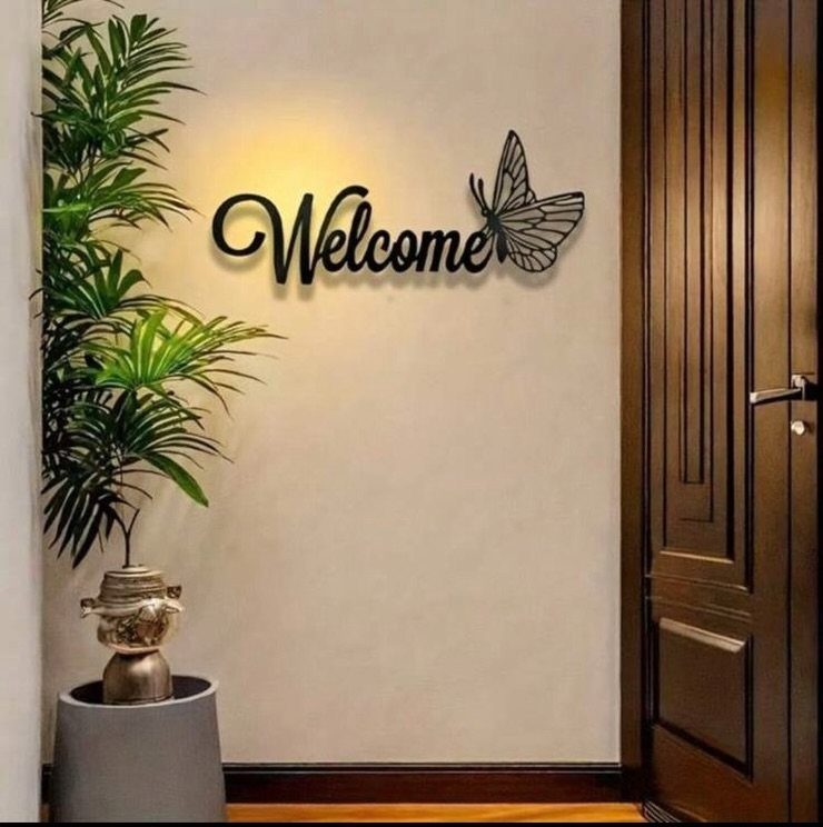Black cursive Welcome sign with butterfly on a white wall by a door