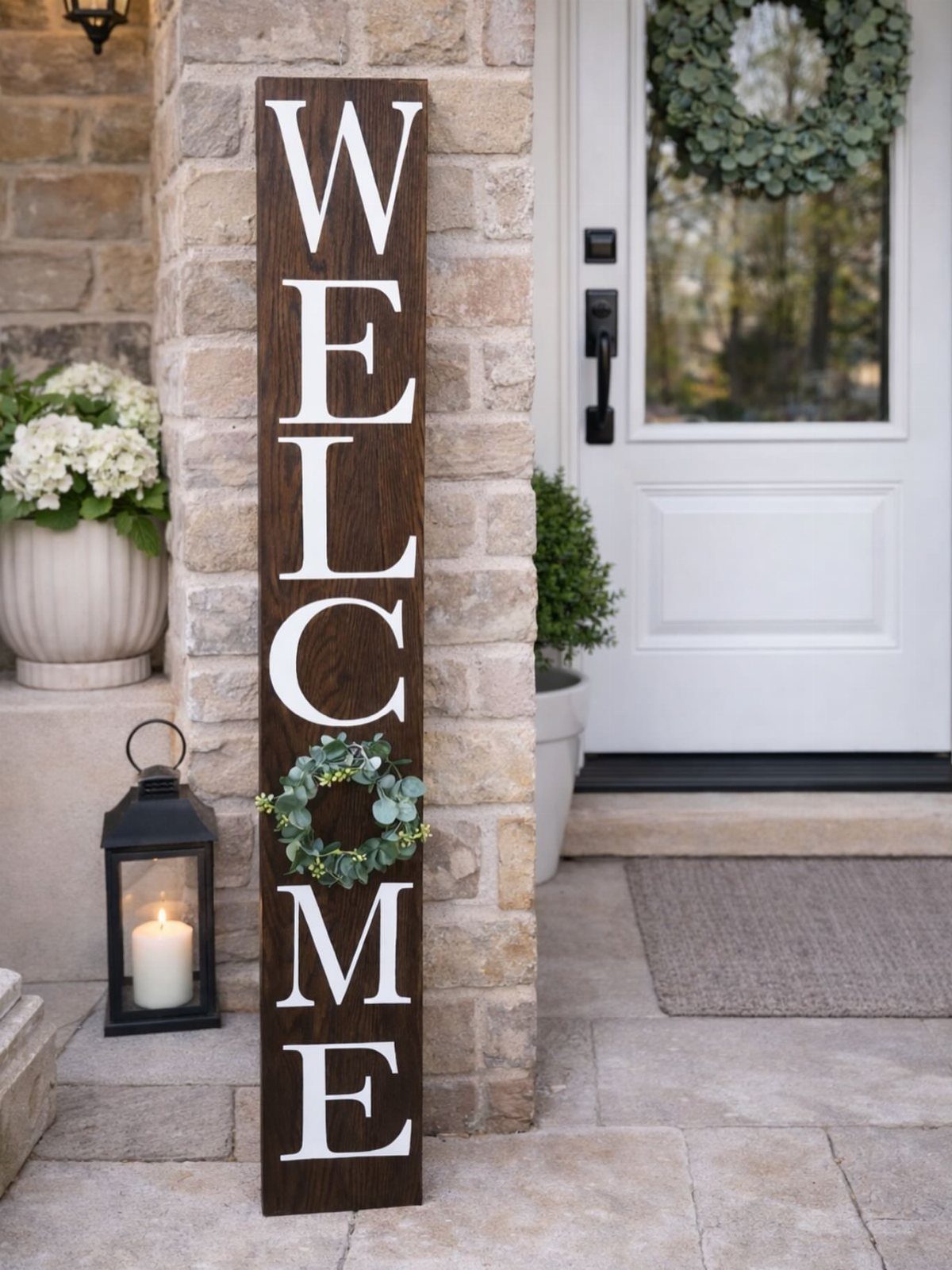 Tall wooden welcome sign with white letters and a wreath on a porch