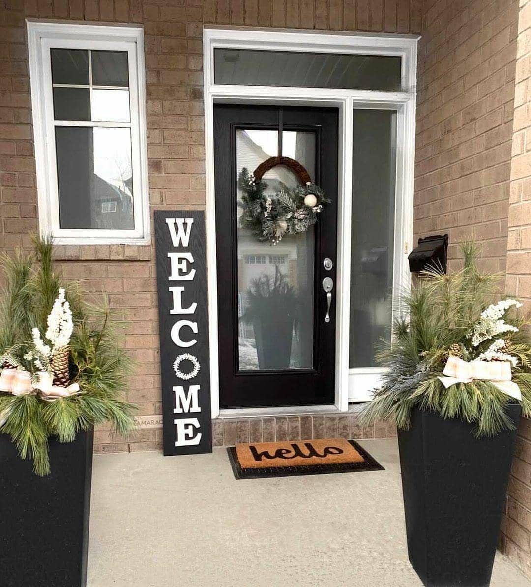 Vertical black wooden welcome sign standing on a porch next to a black door.