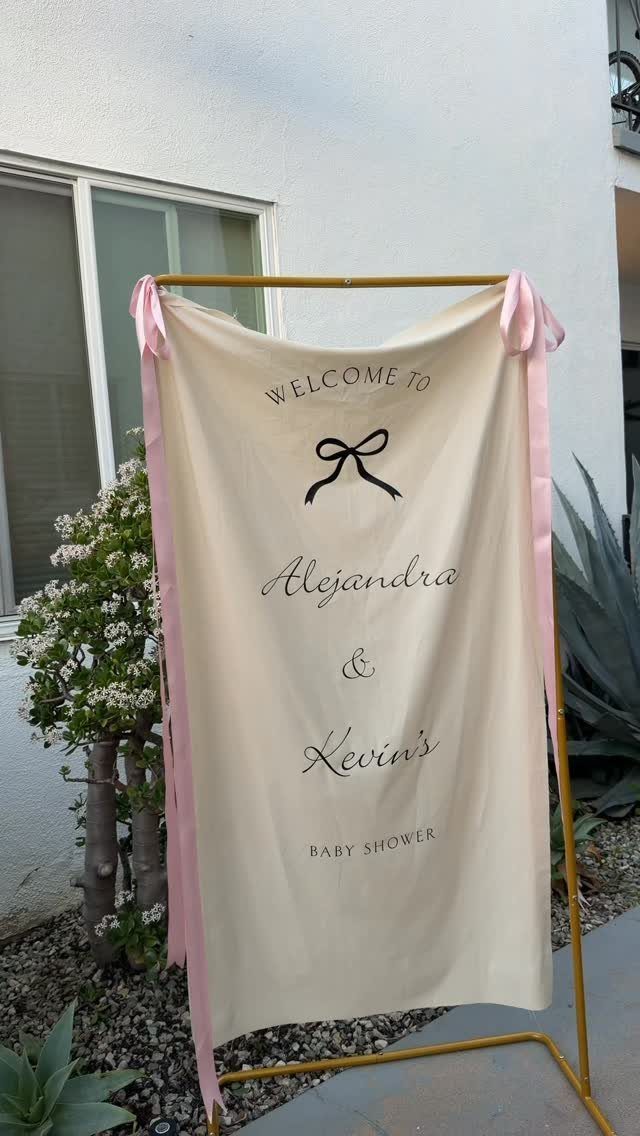 Cream fabric welcome sign for a baby shower on a gold metal frame.
