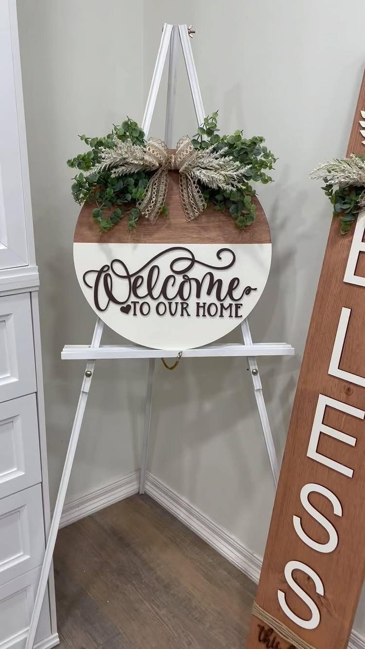 Circular wooden welcome sign with greenery on a white easel in a room