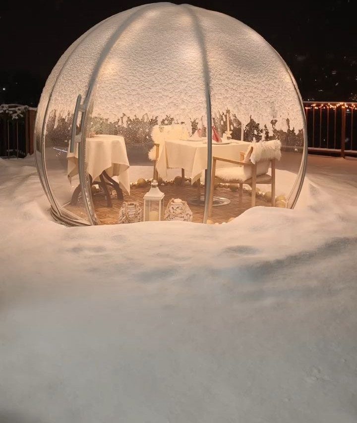 Transparent dome igloo in snow with a romantic dinner table set inside