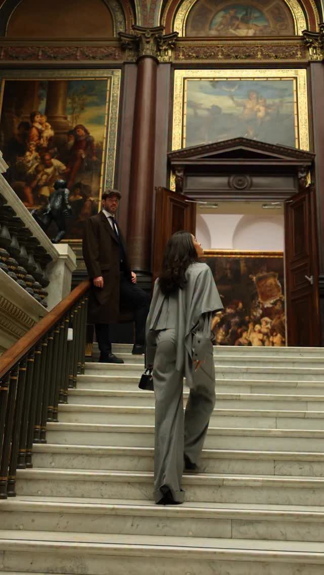Couple in formal wear standing on marble stairs in a grand art gallery.