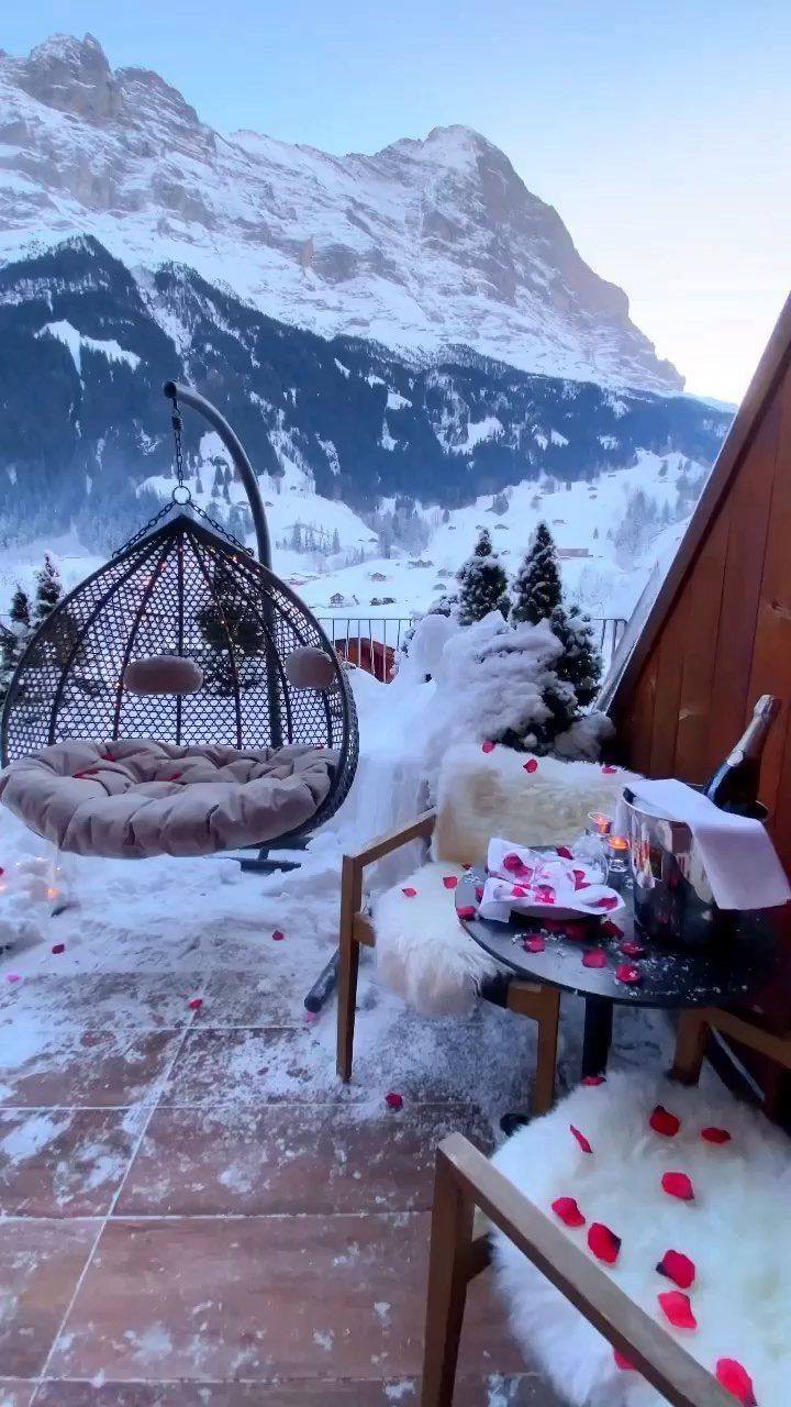 Romantic snowy terrace with rose petals, champagne, and mountains in the background.