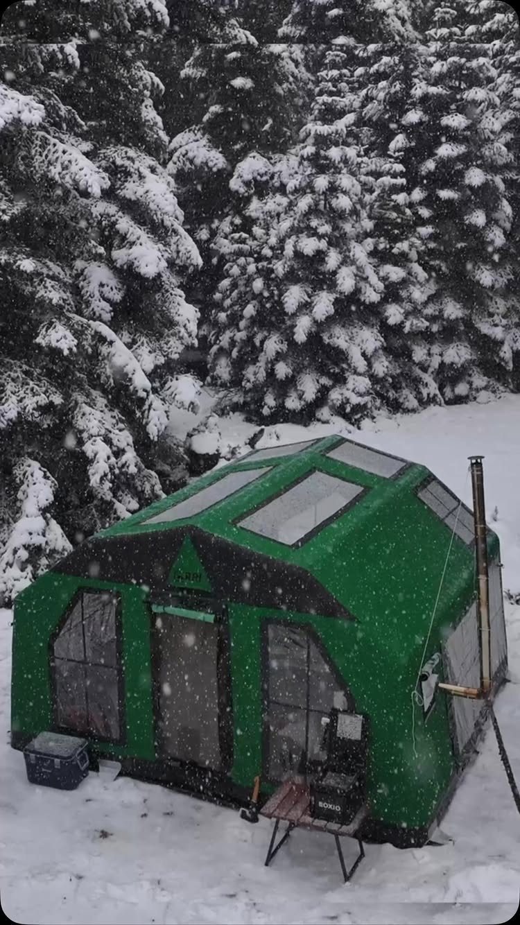 Green winter camping tent with stove pipe in a snowy evergreen forest