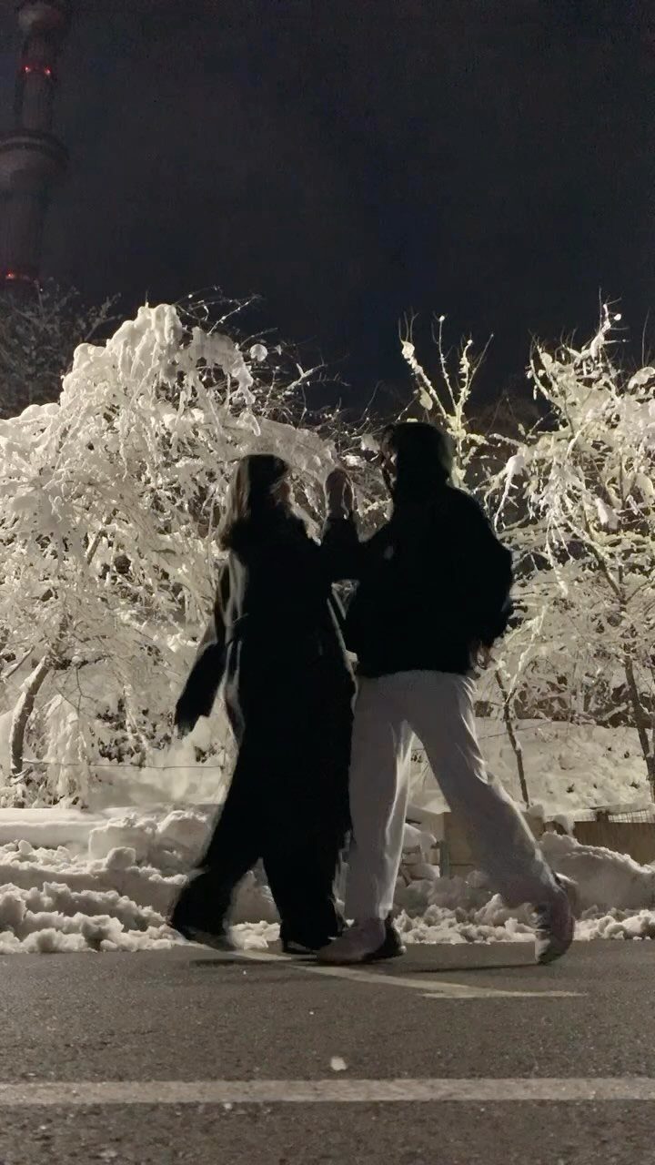 Couple walking hand-in-hand at night past glowing ice-covered trees and snow.