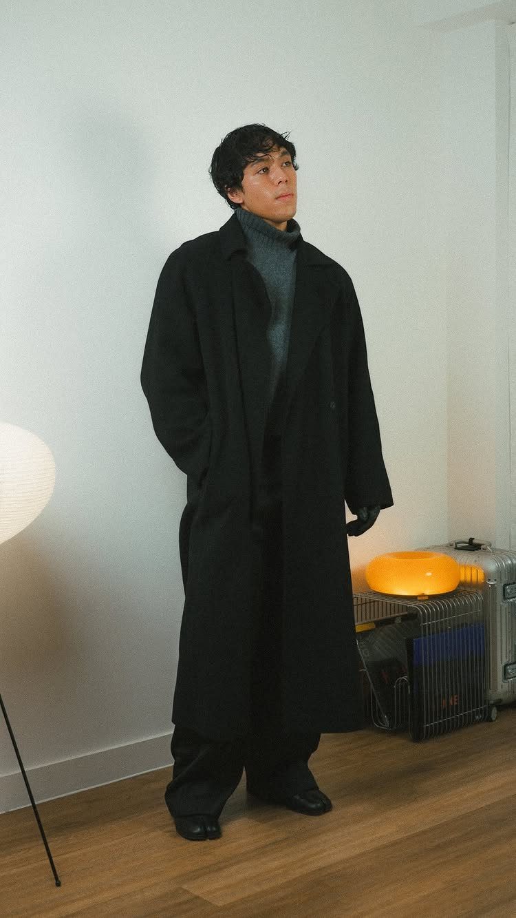 Person wearing a long black coat over a grey turtleneck knit sweater.