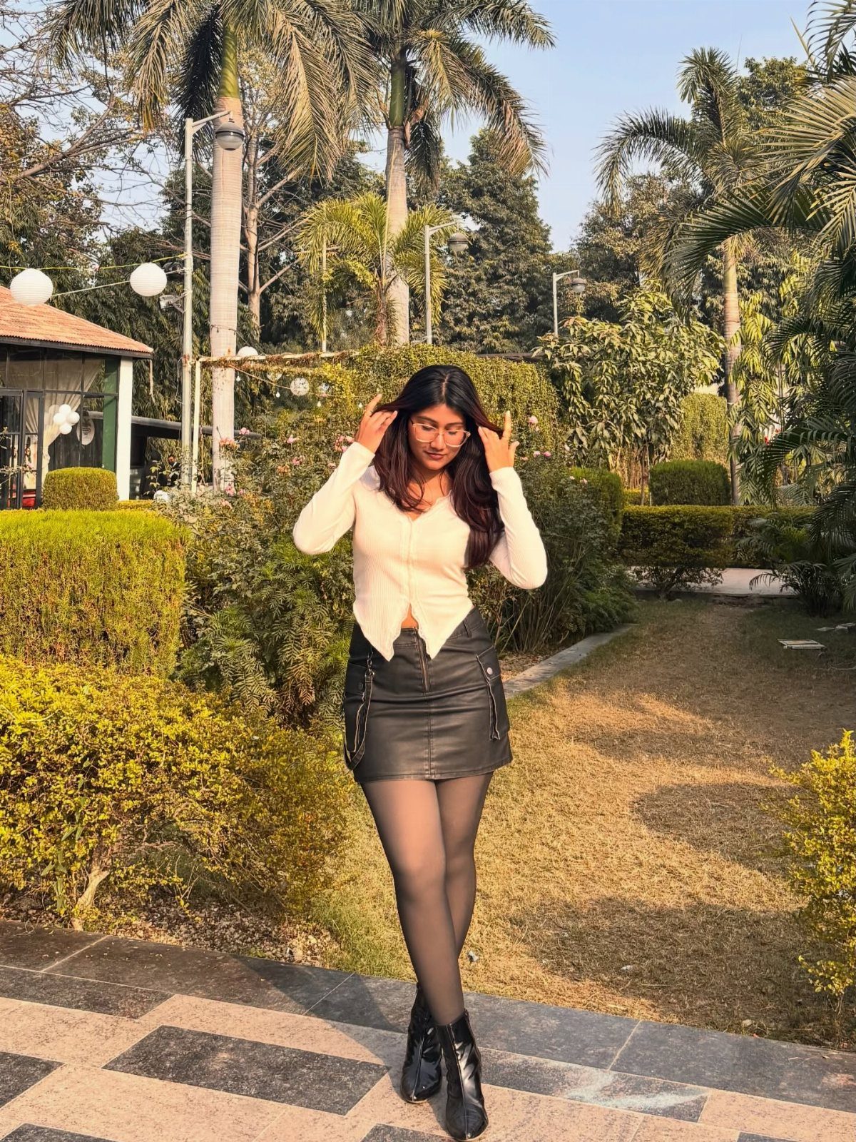 Woman wearing a black leather mini skirt, white top, and black high heels.