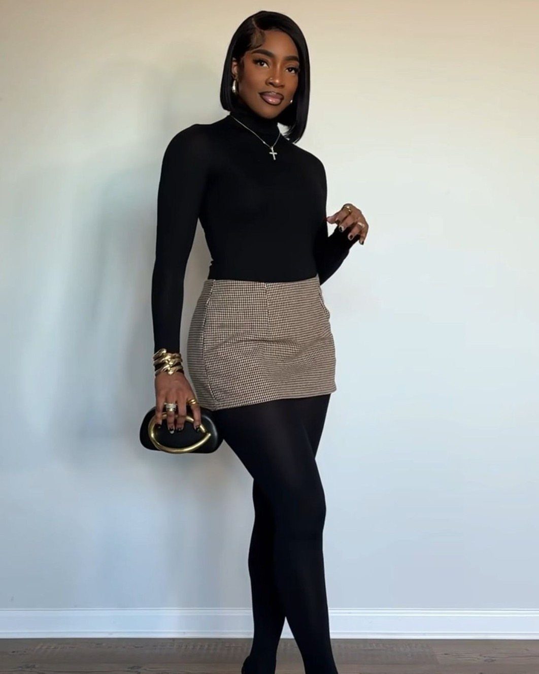 Woman wearing a houndstooth pencil skirt with black tights and a black turtleneck.