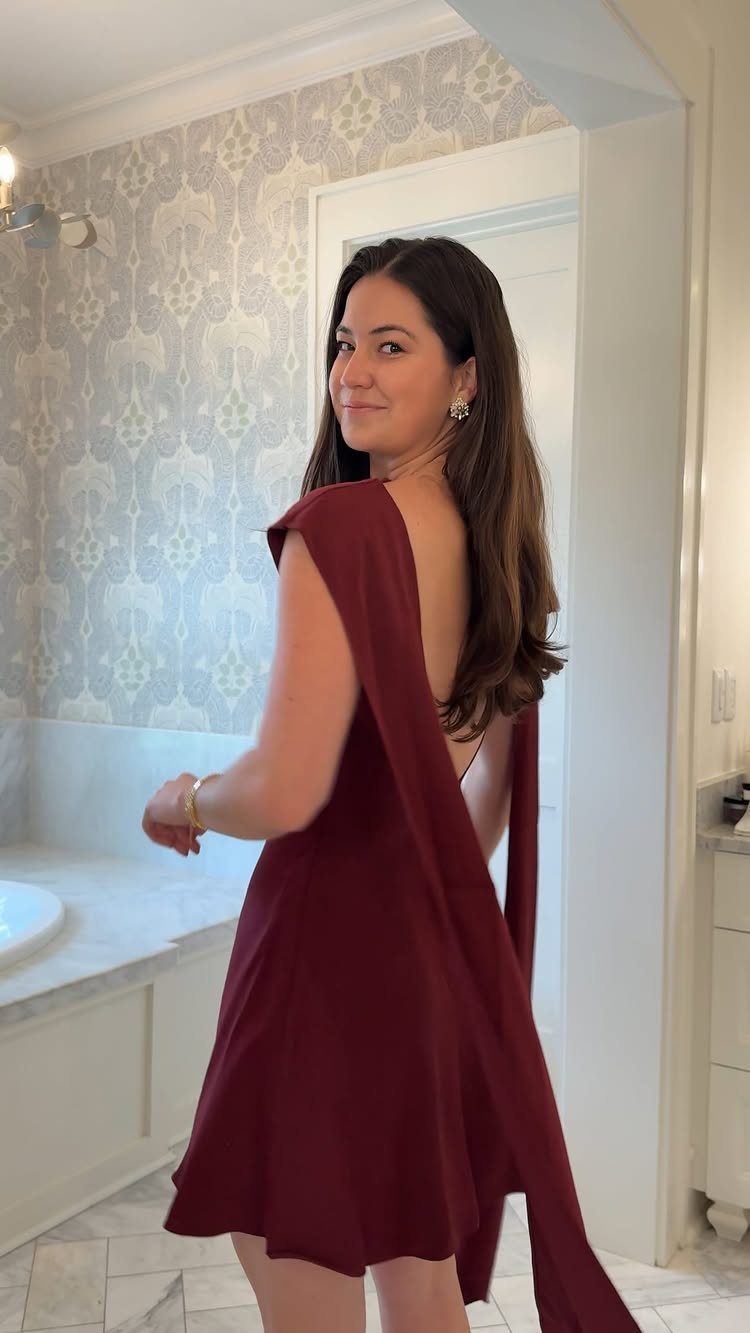 Woman in a short deep red cocktail dress posing in a bathroom
