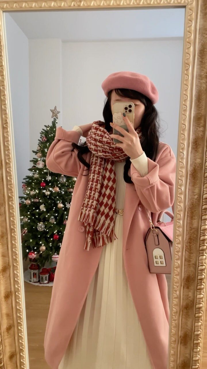Woman in pink coat, beret, and checkered scarf posing by a Christmas tree.