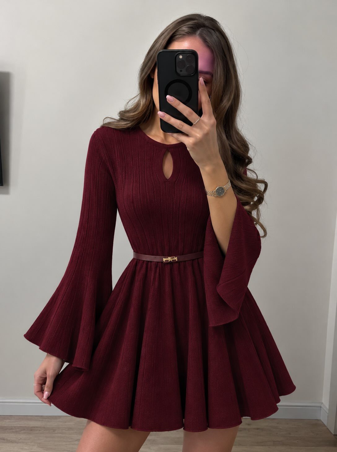 Woman in a short burgundy ribbed dress with bell sleeves and brown belt.