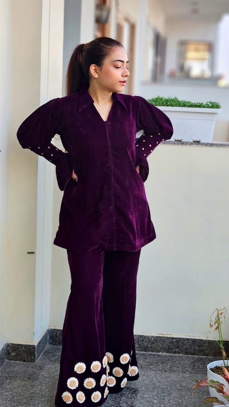 Woman in a purple velvet matching top and pants set with daisy embroidery.